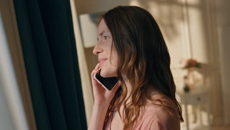 girl talking mobile phone coming to window closeup. smiling woman in sunlight