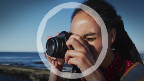 animation of circles over biracial woman taking photo with camera by sea