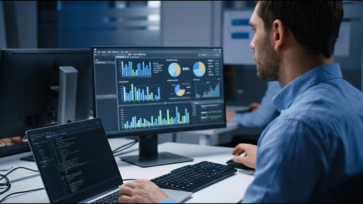 Programvareutvikler analyserer diagrammer og koder data på flere dataskjermer på et moderne kontor
