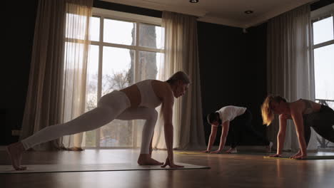 In-Zeitlupe-Macht-Eine-Gruppe-Von-Frauen-Gemeinsam-Yoga-Unterschiedlichen-Alters-Und-Gewichtsklassen.-Dünne-Und-Dicke-Frauen-Im-Fitnessstudio-Morgens-In-Der-Sonne.-Der-Glanz-Der-Sonne-Auf-Dem-Boden