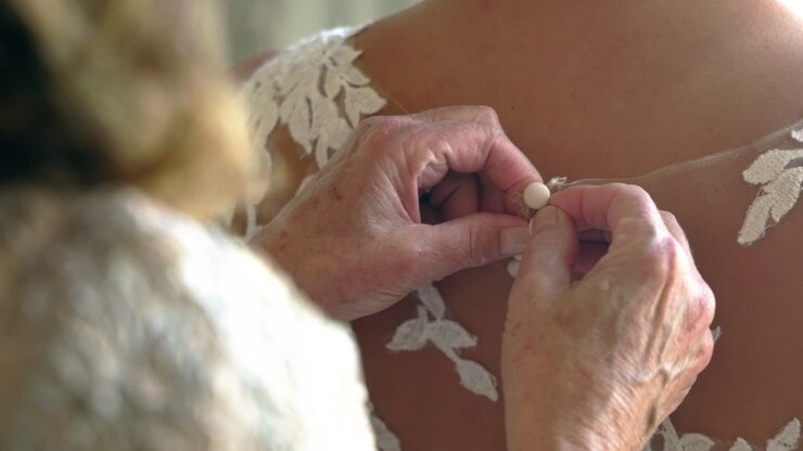 Woman helping bride on wedding day put her dress on, buttoning up the back of her dress