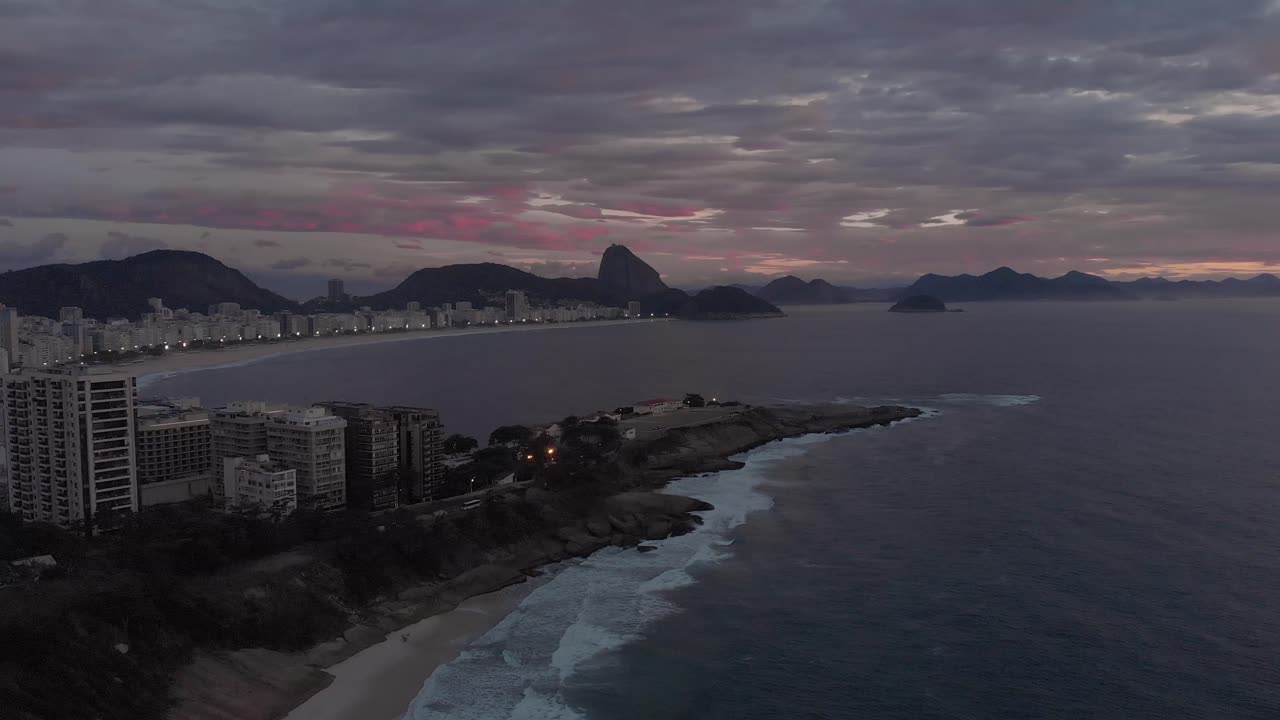 descenso lateral aéreo que muestra el amanecer coloreando las nubes sobre la playa de copacabana con el fuerte de copacabana y la pequeña playa en primer plano en río de janeiro
