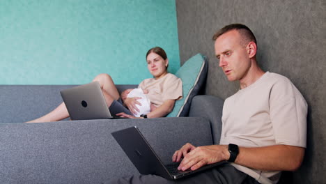 Modern parents of a newborn work at home remote. Woman with baby in hands uses laptop and speaks to her husband.