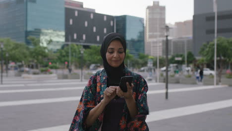 Retrato-De-Una-Elegante-Mujer-Musulmana-Madura-Enviando-Mensajes-De-Texto-Navegando-Usando-Una-Aplicación-De-Redes-Sociales-Para-Teléfonos-Inteligentes-Disfrutando-Charlando-En-El-Fondo-De-La-Ciudad-Urbana-Al-Atardecer