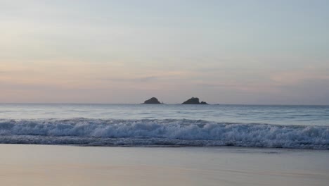 ultra slow motion shot of waves breaking and swashing at beach with beautiful colourful sky at dusk in asia