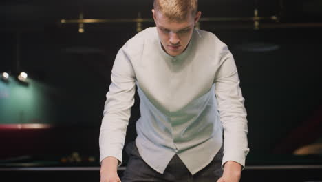 close-up of focused player in white shirt arranging colorful billiard balls in triangle formation on vibrant green pool table under warm ambient lighting, in modern billiard room