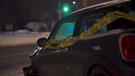 secuelas de un accidente automovilístico en una noche nevada de invierno con un pequeño vehículo de pasajeros dañado envuelto en cinta de precaución