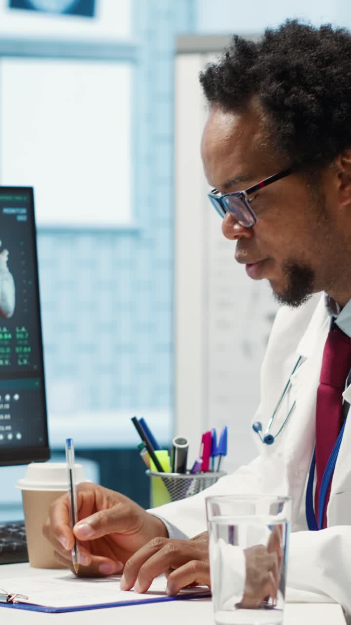 African American Doctor Writing on Clipboard and Looking at Medical Monitor