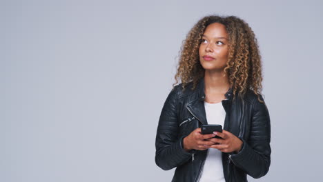 Foto-De-Estudio-De-Una-Mujer-Con-Chaqueta-De-Cuero-Enviando-Mensajes-De-Texto-Por-Teléfono-Móvil-En-Cámara-Lenta