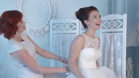 bride's friend helps the bride wear a wedding dress they laugh then the bride falls