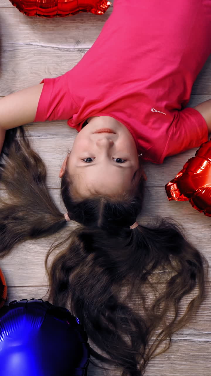 Cute girl lying on floor with balloons. Top creative view of little girl on floor with balloons in form of heartin