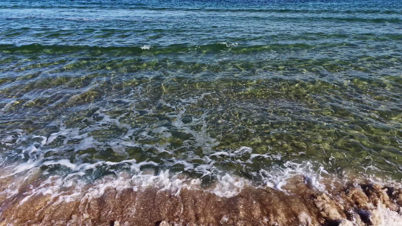 Waves gently lap the shore at a serene beach during a sunny afternoon, inviting relaxation and contemplation by the water's edge