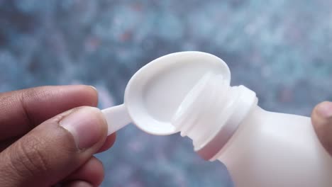 verter líquido de una botella blanca con una cuchara medidora