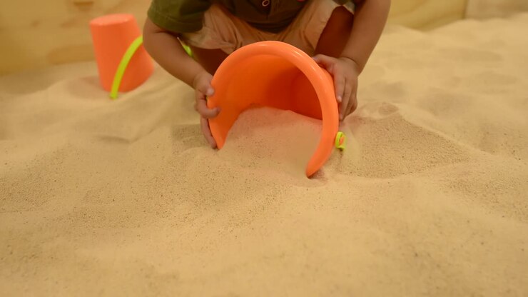 Inquadratura dal basso di un bambino piccolo che gioca con sabbia e un secchiello in una sabbiera in un parco giochi
