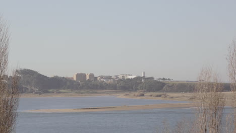 Weitwinkelaufnahme-Des-Flusses-Douro,-Mit-Einigen-Gebäuden-In-Vila-Nova-De-Gaia-Im-Hintergrund-Und-Einigen-Zweigen-Im-Wind-Im-Vordergrund