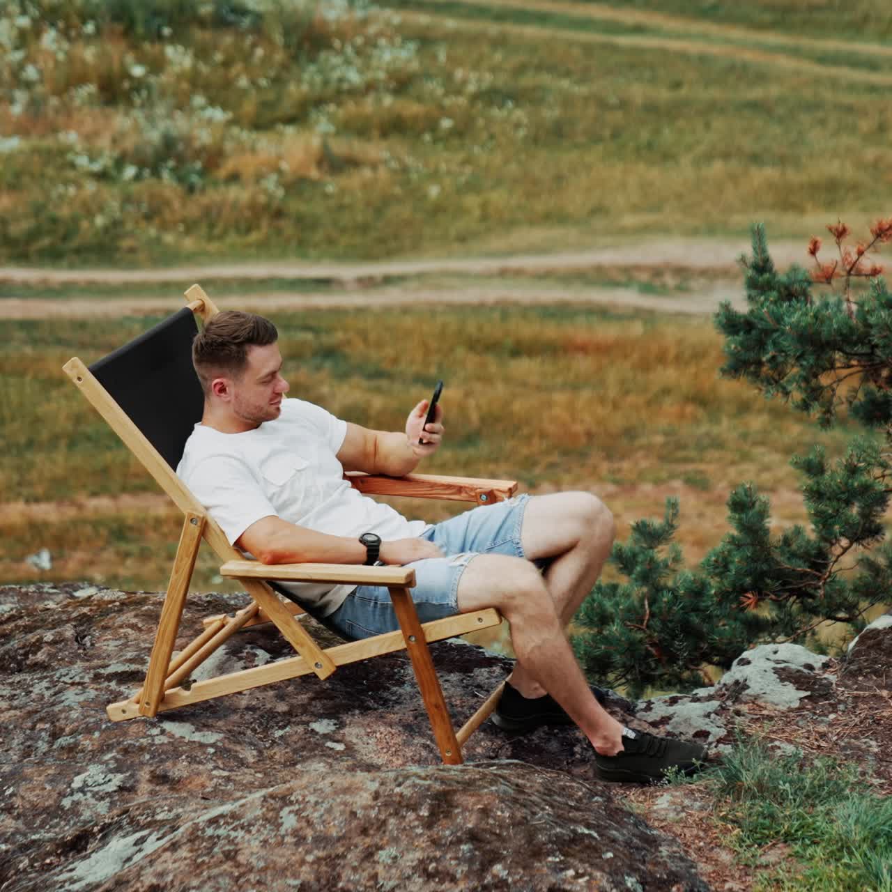 Uomo che si riposa nella natura. Un uomo caucasico è seduto su una comoda sedia pieghevole sulla roccia mentre parla al telefono. Vista dall'alto