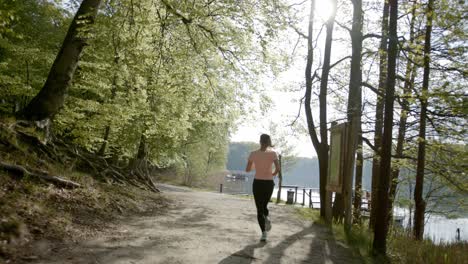 Runner-running-on-dirt-path-through-woods-near-lake-on-sunny-day