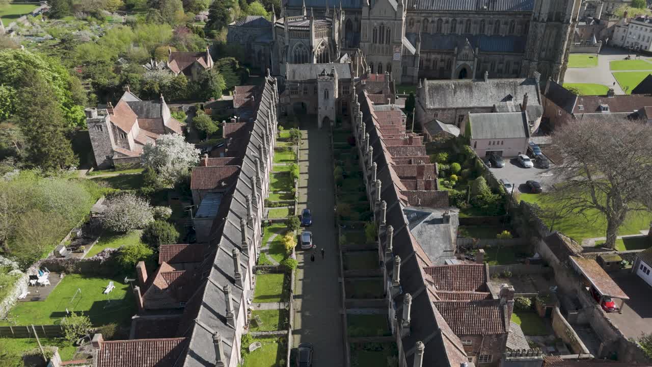 Aerial view of medieval Vicars' Close with parallel stone cottages, tall chimneys and a green central lane converging toward a Gothic cathedral, illustrating preserved heritage living