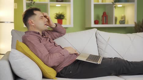 the man looking at the laptop while lying down is depressed by what he sees on the screen.