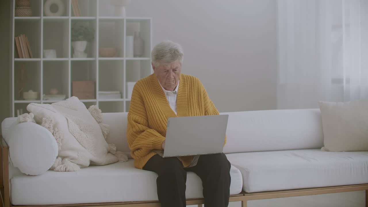 Senior woman with gray hair make video call using laptop at home. Elderly woman having a video call with family smiling and waving. COVID 19 Stay connected. Online chatting with friends