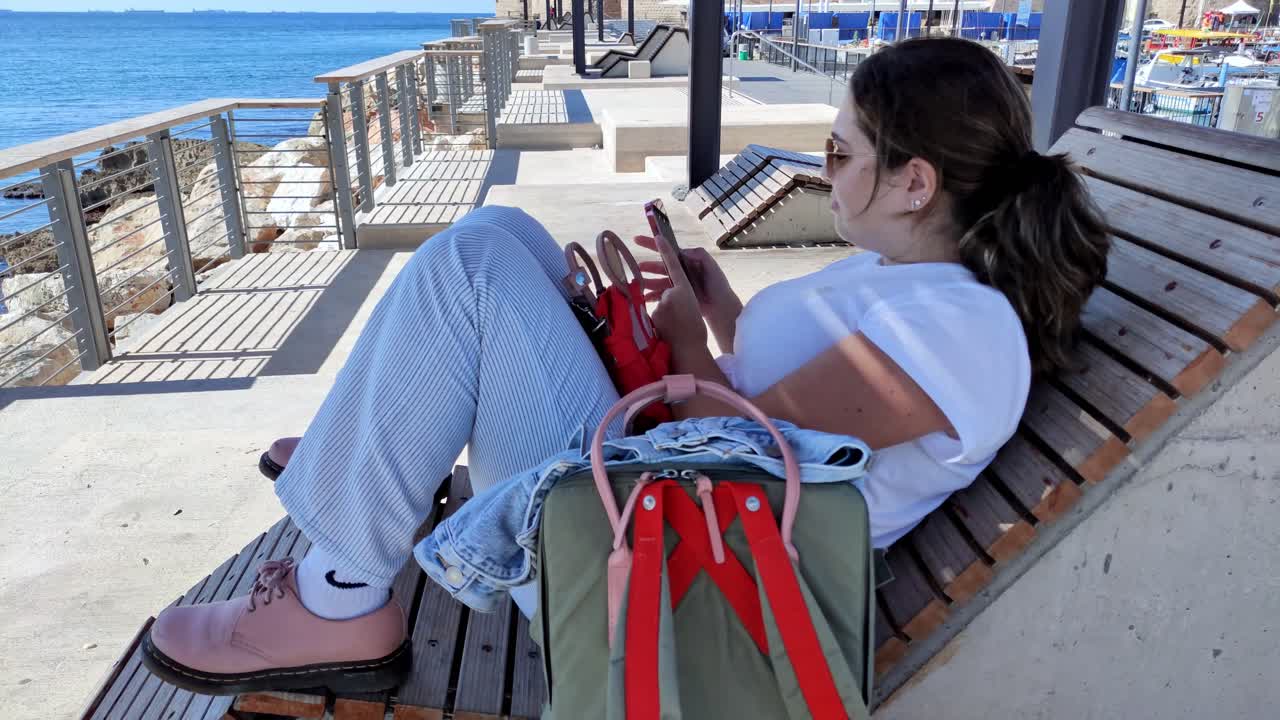 Donna che si rilassa sul lungomare usando lo smartphone ad Akko