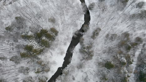 high altitude aerial view from drone looking down on magical winter snowy countryside landscape passing over forest, field and homes blanketed in fresh white snow