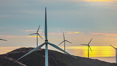 closeup of rotating windmills above sunset skyline and mountains time lapse sun background, motion of renewable energy fans in countryside landscape