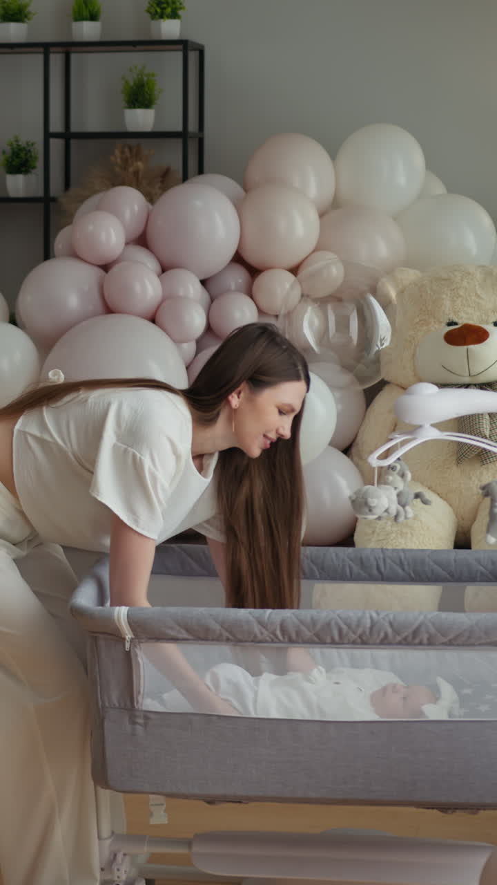 Madre che adagia delicatamente un neonato nella culla, circondato da palloncini e orsetti di peluche, per celebrare la nascita