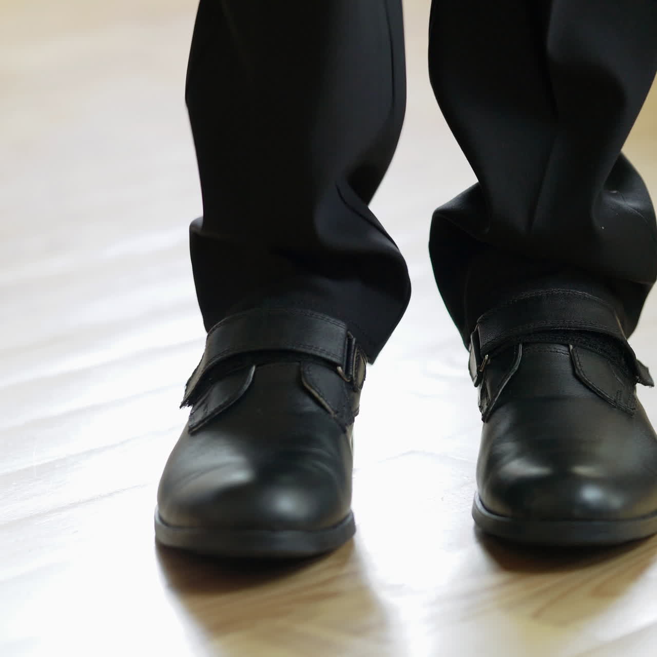Male's legs wearing elegant shoes come into the room, stand for a while and go away. A pair of stylish shoes on a man in black suit on the floor inside