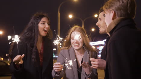 grupo de amigos con ropa elegante sosteniendo bengalas en la calle después de la fiesta de año nuevo