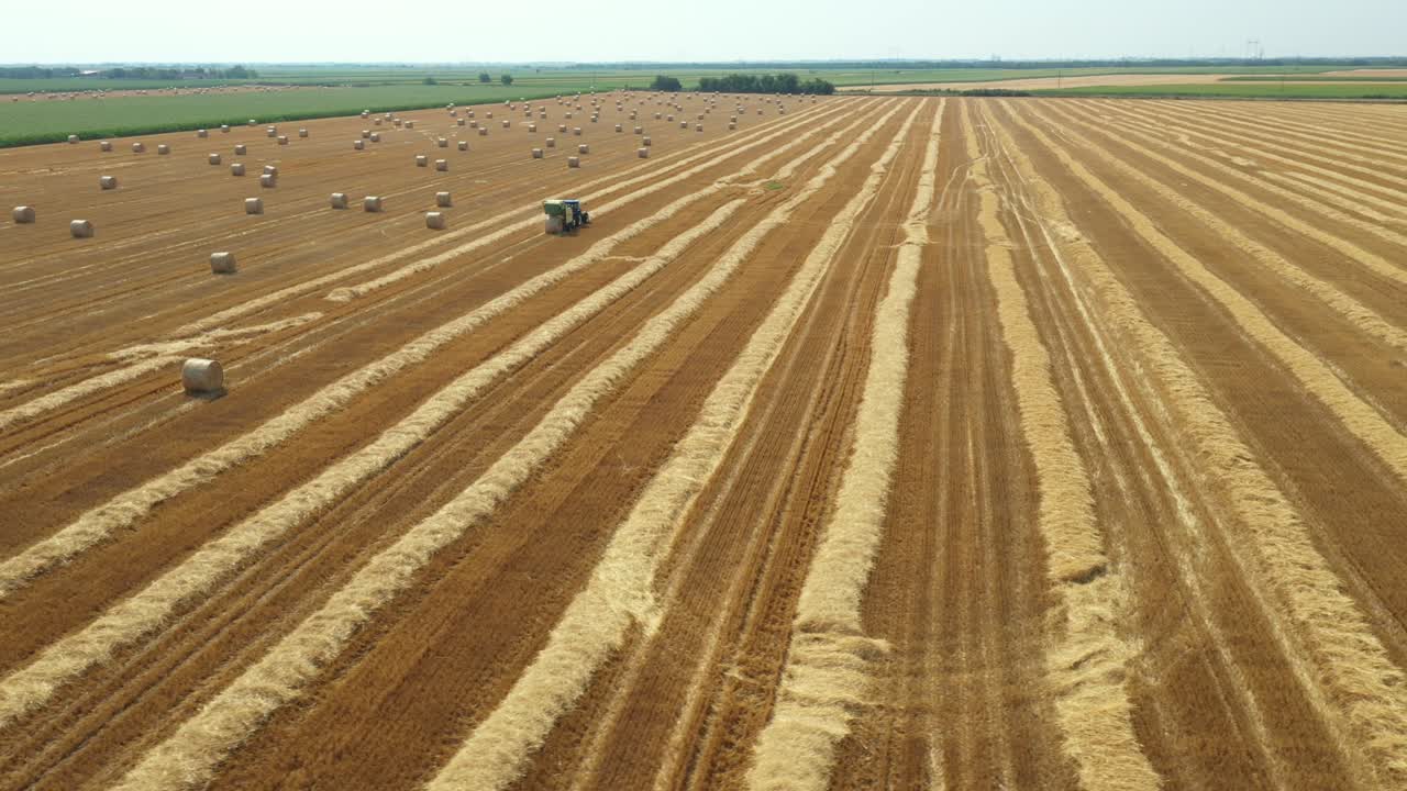 Aerial circling view of tractor tow trailed bale machine to collect straw from harvested field