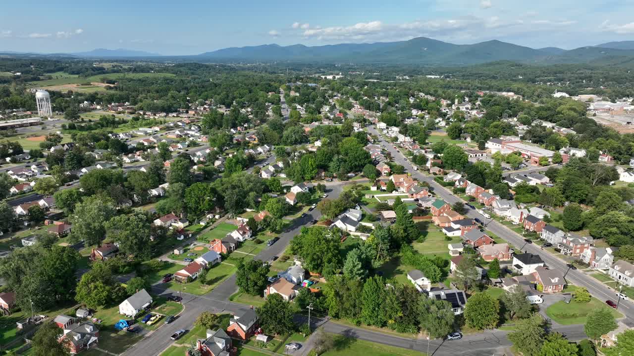Quiet and quaint small neighborhood city of America with green trees, hills snd water tower in distance. Descend drone wide shot on sunny summer day. Virginia, USA