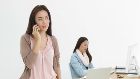 creative businesswoman talking on phone with colleague behind her