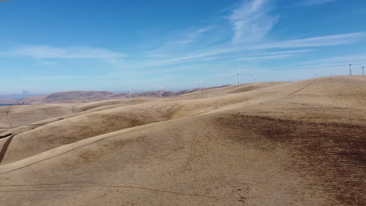Traveling drone footage moving in on energy producing windmills in the rolling hills of California