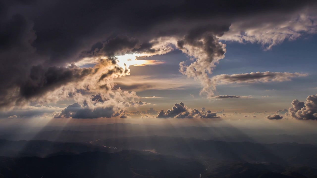 Il sole che filtra attraverso una grande e scura coltre di nuvole rivela raggi crepuscolari sopra le creste delle montagne