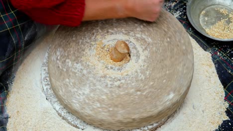 woman is grinding wheat by hand in stone mill