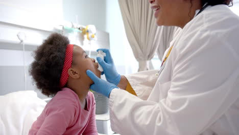 Doctora-Afroamericana-Dando-Inhalador-Y-Medicamento-A-Una-Niña-En-La-Habitación-Del-Hospital,-Cámara-Lenta