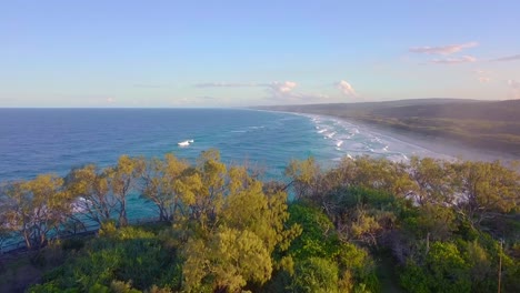 Aufschlussreiche-Schnelle-Luftaufnahme-Eines-Wilden-Strandes-Und-Türkisblauen-Ozeans-Mit-Wellen-Bei-Sonnenuntergang