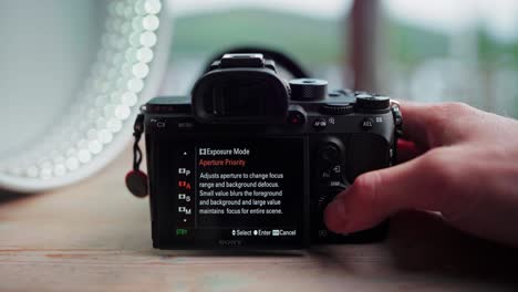 hand adjusting the settings of a digital camera on wooden table - close up