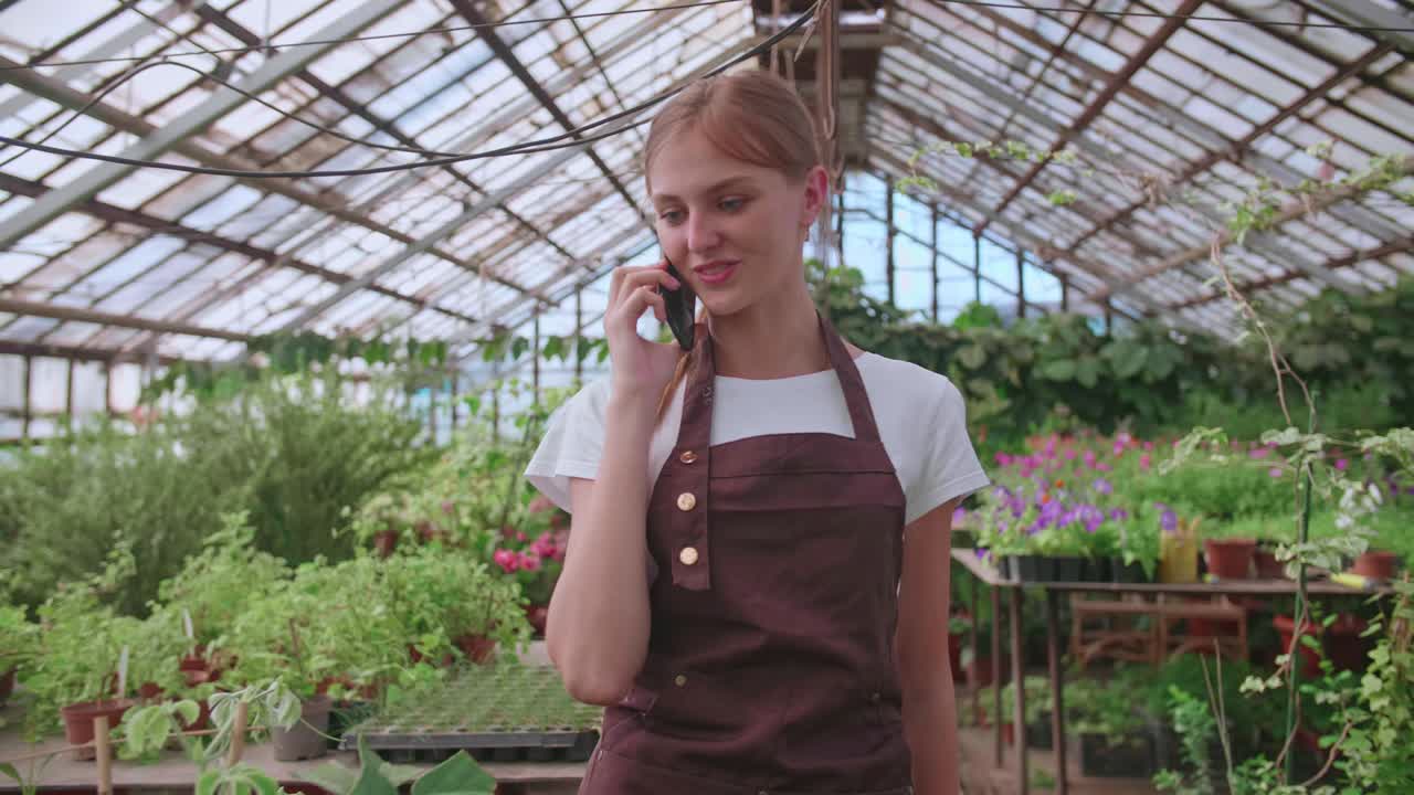 어린 소녀 유치원 직원과 꽃 온실은 전화로 클라이언트와 이야기합니다.