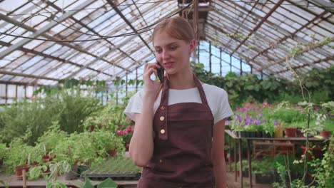 una joven trabajadora de un vivero y un invernadero de flores habla con un cliente por teléfono