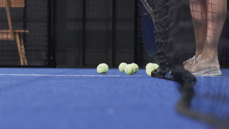 White woman stepping behind net on padel court clearing yellow balls using racket, copy space