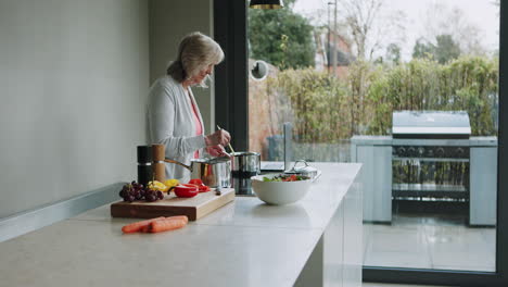 senior woman cooking in the kitchen with a laptop