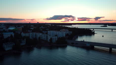 aerial view of the lauttasaarensilta bridge and the lauttasaari cityscape, dusk in helsinki, finland - tracking, drone shot