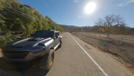 reverse fpv view of an off roader jeep running on an isolated countryside road during bright sunny day