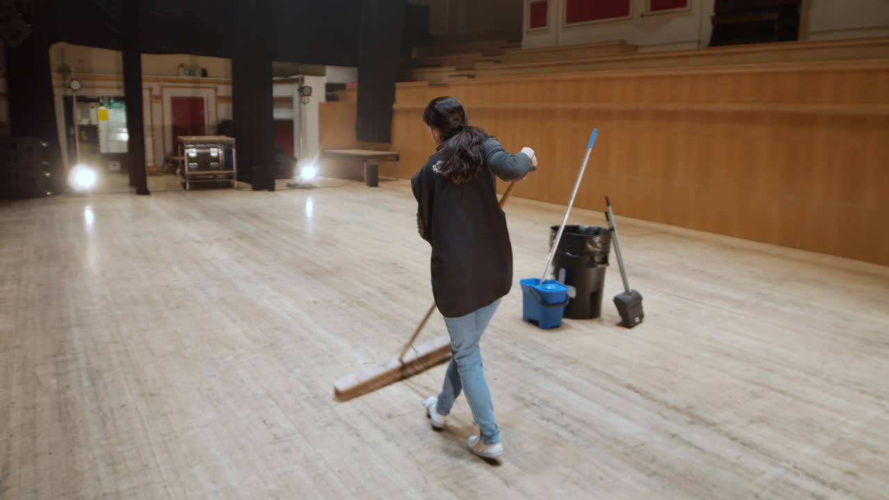 Unrecognizable female cleaner sweeping a stage floor in a theater.