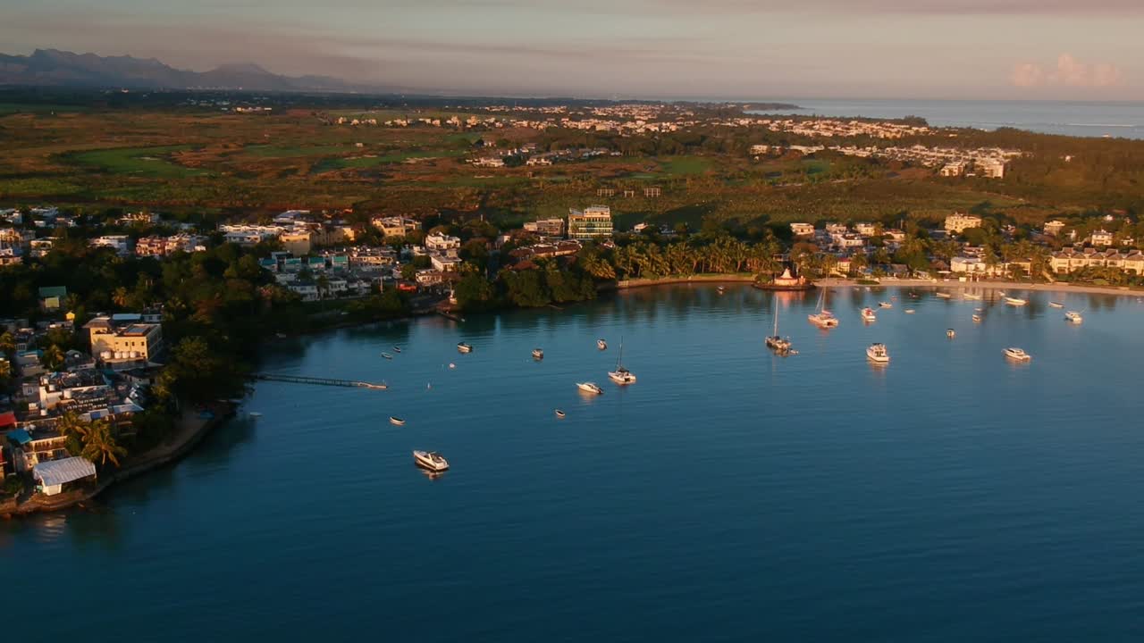panorámica aérea de gran bahía, con barcos anclados, casas, tierra verde y el océano y las montañas en el fondo