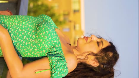 glamorous-fancy-women-model-with-messy-brown-hair-wearing-green-cute-dress-leaning-on-a-fence-relaxing-her-head-back-with-closed-eyes-and-looking-straight-into-camera-slow-motion-vertical-cinematic