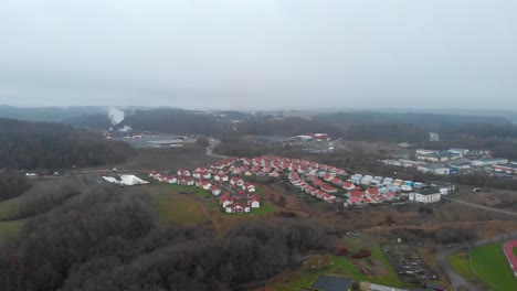 daytime view small village with identical white houses red rooftops next to factory, aerial