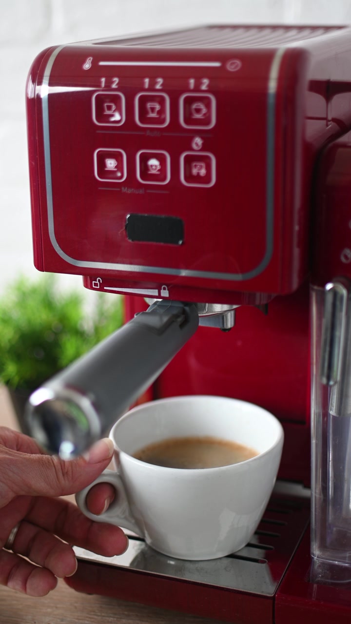 Mão pegando xícara de café da máquina de expresso em cozinha moderna.